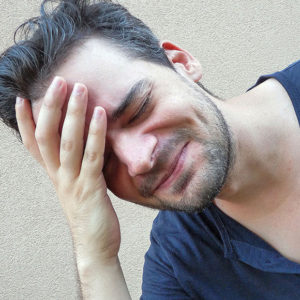A man holds his head as if he is uncomfortable.