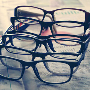 six pairs of glasses are nestled against each other on top of a newspaper