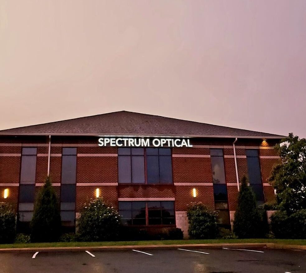 A lit Spectrum Optical sign illuminates the Bridgeport office with a pink and purple sunset in the background. Quality eye care starts here!