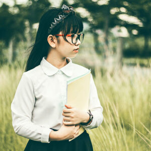 A girl wearing glasses holds a notebook in front of a field of wheatgrass.
