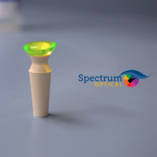 A green contact lens rests on a contact lens plunger beside the Spectrum Optical logo.