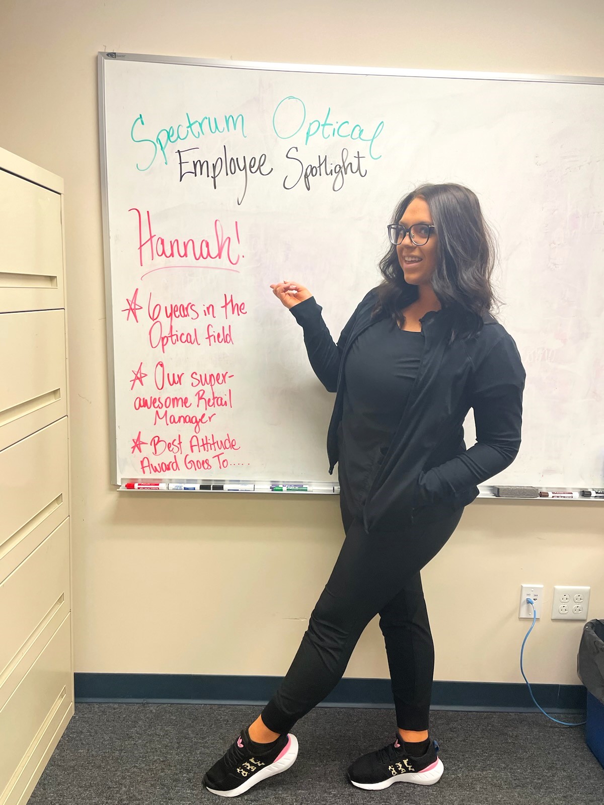 February Employee Spotlight (our Retail Manager, Hannah) stands in front of a white board pointing to her name.