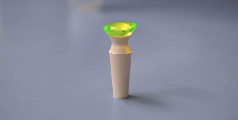 A contact lens filled with solution rests on a contact lens insertion plunger.